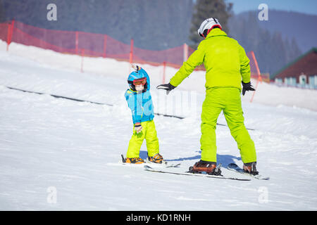 Lektion am Ski Schule: Lehrer Unterricht wenig Skifahrer wie Drehungen, Jungen tun Übung auf der Piste im Kinderbereich zu machen Stockfoto