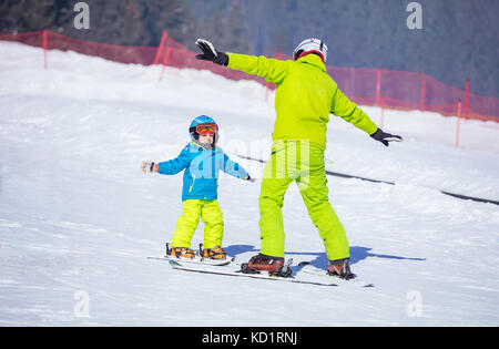 Lektion am Ski Schule: Lehrer Unterricht wenig Skifahrer wie Drehungen, Jungen tun Übung auf der Piste im Kinderbereich zu machen Stockfoto