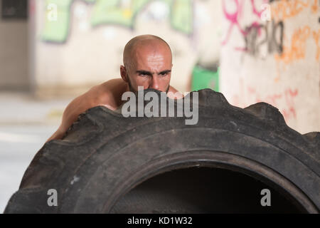 Junger muskulöser Mann mit LKW-Reifen dabei Crossfit Stil Training Reifen drehen über Stockfoto