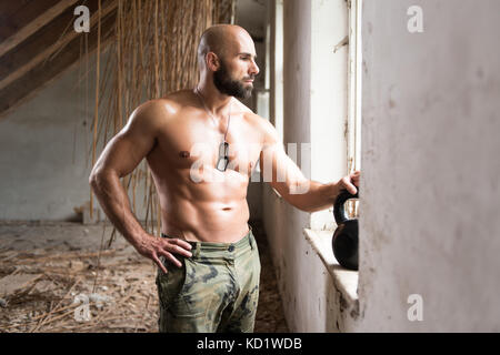 Man Trainieren mit einem Wasserkocher Bell- und Biegungsspiel Muskeln - Muskulatur athletische Bodybuilder Fitness Modell Übungen in Ruinen Stockfoto