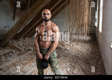 Man Trainieren mit einem Wasserkocher Bell- und Biegungsspiel Muskeln - Muskulatur athletische Bodybuilder Fitness Modell Übungen in Ruinen Stockfoto
