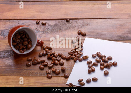 Genügend Schlaf aus einer Tasse Bohnenkaffee. Kaffee Körner aus dem Cup über Papier und broun Holz- Hintergrund Stockfoto