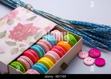 Bunte makronen in einer Geschenkbox mit Blumen und Schaltflächen auf grauem Hintergrund. Süße macarons. Für text Stockfoto