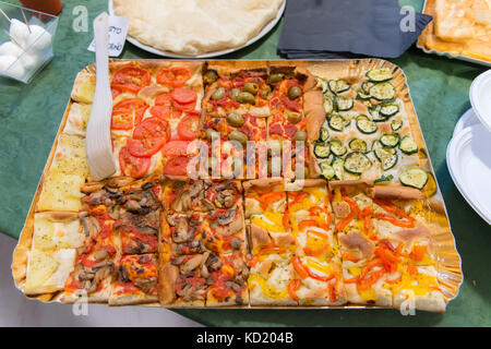 Stücke von Pizza schneiden in Quadrate, verschiedene Zutaten wie Pilzen, Paprika, Oliven und Gurken Stockfoto