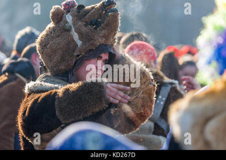 Pernik, Bulgarien - Januar 27, 2017: maskierte Teilnehmer im Pelz tragen Maske ist heben seine Maske, lächelnd und mit seinem Gehilfen an surva, die internati Stockfoto