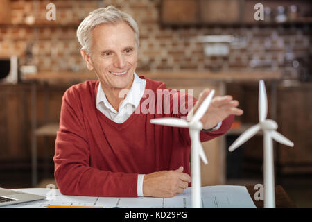 Freudige älterer Mann eine Hand gegen Wind Turbine Modelle Stockfoto