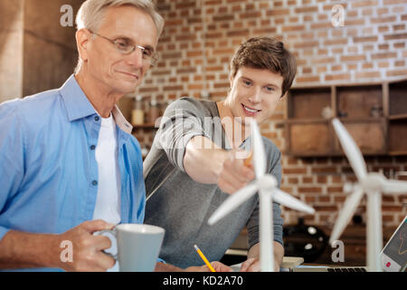 Angenehmer junger Mann an Windkraftanlagen, die auf seinen Mentor Stockfoto
