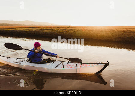 Mitte der erwachsenen Frau Kajakfahren auf dem Fluss bei Sonnenuntergang, Morro Bay, Kalifornien, USA Stockfoto