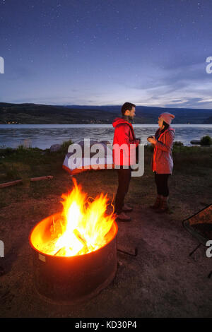 Paar in der Nähe von Zelt und Lagerfeuer. In der Abenddämmerung, trinken heiße Getränke Stockfoto