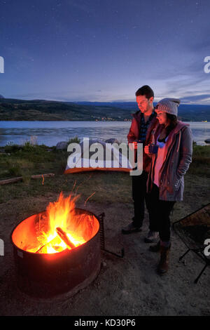 Paar in der Nähe von Lagerfeuer. In der Abenddämmerung, trinken heiße Getränke Stockfoto