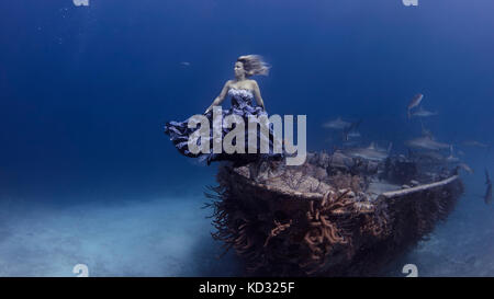 Unterwasseransicht der Frau in lila Kleid von schiffbrüchigen Boot balanciert, Bahamas Stockfoto