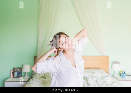 Junge Frau auf dem Bett Gähnen und Strecken Stockfoto