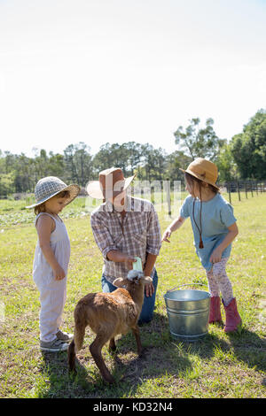 Mutter und zwei Kindern auf der Farm, mit der Flasche füttern junge Ziege Stockfoto