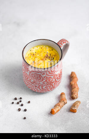 Styled Lager minimalistischen lifestyle Foto einer Latte mit Gelbwurz Kurkuma Wurzel, schwarze Pfefferkörner und Zimt in einer handgefertigten Becher auf Beton. Stockfoto