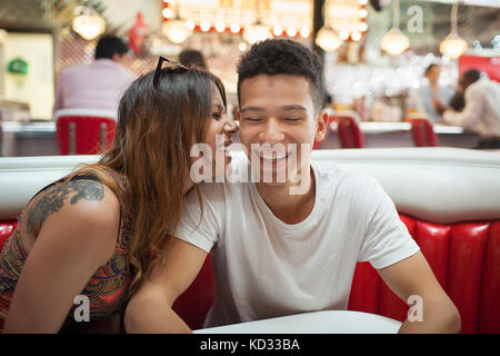 Junges Paar in Diner sitzen, junge Frau das Flüstern im Ohr des Menschen, Lachen Stockfoto