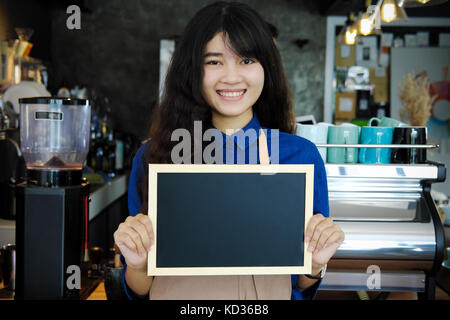 Portrait von lächelnden asiatischer barista Holding leere Schiefertafel Menü im Coffee Shop. Cafe Restaurant Service, Inhaber kleiner Unternehmen, die Lebensmittel- und Getränkeindustrie Stockfoto