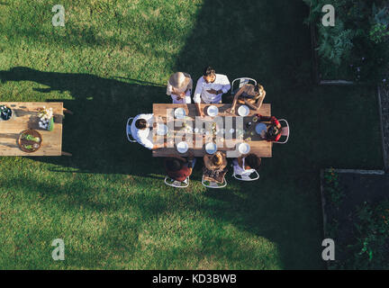 Luftaufnahme von Freunden genießen Sie Mahlzeiten im Party im Freien. Gruppe von Menschen um einen Tisch im Restaurant im Garten sitzen und essen zusammen.