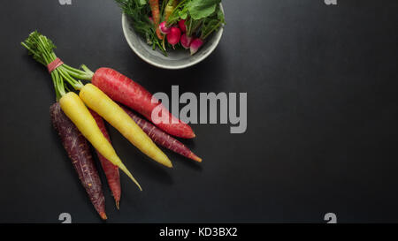 Bunte Karotten und Radieschen zusammen am Tisch neben einer Schale dill Blätter, Spinat und Radieschen gebündelt. Stockfoto