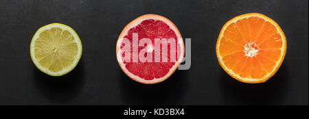 Blick von oben auf die eine Hälfte der Orange, Grapefruit und Zitrone auf einem schwarzen Hintergrund angeordnet. Frische Zitrusfrüchte. Stockfoto