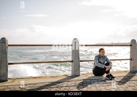 Frau Entspannung nach dem Training auf der Straße durch das Meer. Sportlerin, die Pause nach dem Fitness Training im Freien durch das Meer. Stockfoto