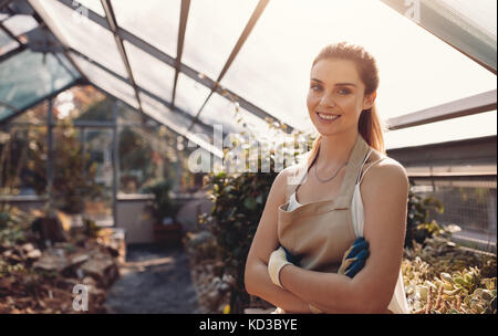 Portrait von selbstbewusste Frau mit Schürze im Gewächshaus. Schöne Gärtner an Gärtnerei arbeiten. Stockfoto