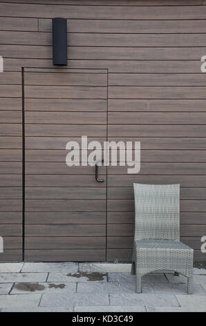 Ein halb versteckt Holztür in der Wand eines Gebäudes, mit einer Lampe über es und ein Stuhl auf seiner Seite. Stockfoto