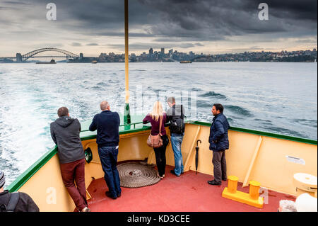 Touristen genießen die Aussicht auf den Hafen von Sydney und die Sydney Harbour Bridge, wie sie nach Manly an Bord der Fähre in einer stürmischen Nachmittag Kreuz. Stockfoto