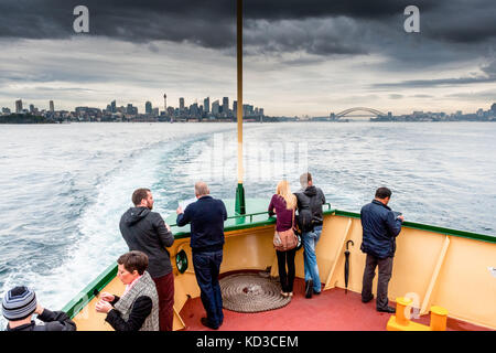 Touristen genießen die Aussicht auf den Hafen von Sydney und die Sydney Harbour Bridge, wie sie nach Manly an Bord der Fähre in einer stürmischen Nachmittag Kreuz. Stockfoto