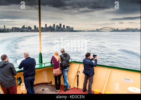 Touristen genießen die Aussicht auf den Hafen von Sydney und die Sydney Harbour Bridge, wie sie nach Manly an Bord der Fähre in einer stürmischen Nachmittag Kreuz. Stockfoto