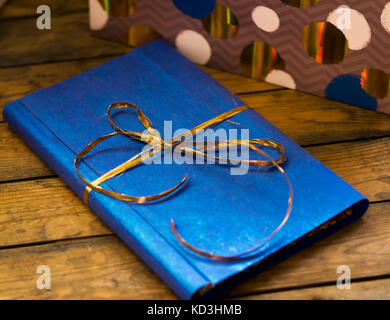 Das Buch liegt auf einer hölzernen Hintergrund, in einem Geschenk, blau Wrapper mit einem Gold Bug Stockfoto