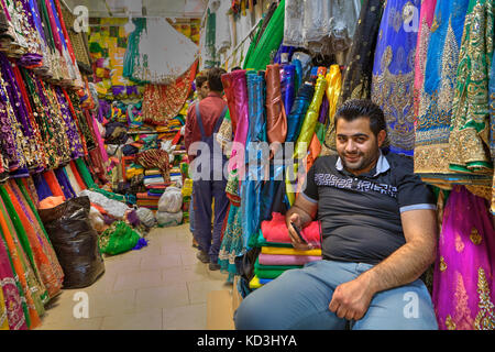 Provinz Fars, Shiraz, Iran - 19. april 2017: Ein reifer iranischer männlicher Verkäufer sitzt entspannt auf einem Stuhl in einem Textilgeschäft und wartet auf Käufer. Stockfoto