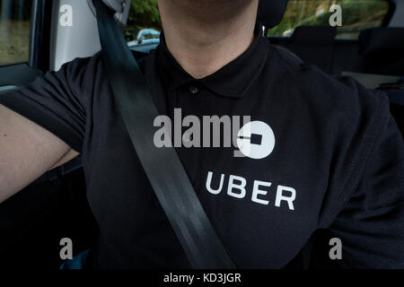 Ein Mann mit einem schwarzen Polo-T-Shirt mit Logo des Unternehmens treibt ein Uber Taxi (nur redaktionelle Nutzung). Stockfoto