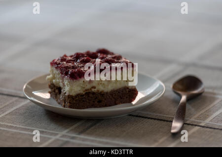Stück Schwarzwälder Kirschtorte mit frischer Sahne und Kirschen, serviert auf einem weißen Teller mit Löffel aus Holz Stockfoto