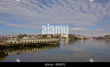 Holzpfähle und Autoreifen eines Piers, die sich im Wasser und auf der Insel mit traditionellen Häusern auf Hundvåg, Insel bei stavanger in einer Norwegischen, spiegeln Stockfoto