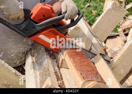 Mann sägt Holz mit orange Kettensäge Stockfoto
