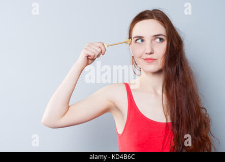 Eine junge hübsche Frau hält eine große Taste neben ihren Kopf und versuchte, ihr Verstand oder Kopf zu öffnen. Das Konzept der Kreativität, Breite des Denkens, Bildung oder Mem Stockfoto