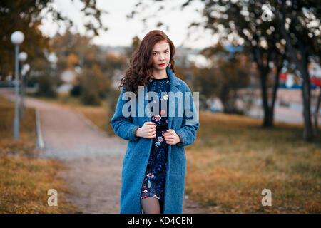 Modische junge Lockige Frau Wandern im Herbst park Tragen von Blue Coat Stockfoto