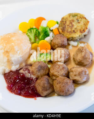 Ein Teller mit IKEA Fleischbällchen, Kartoffelpüree, Sahnesauce, Preiselbeersauce, gemischtem Gemüse und einem Kartoffel-Gemüse-Medaillon (grönsakskaka). Stockfoto