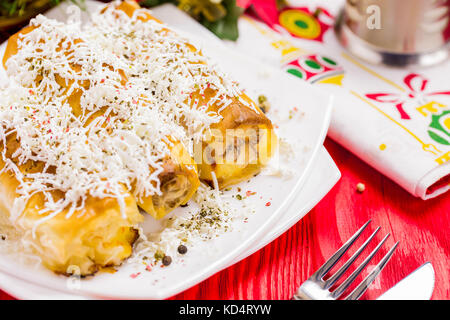 Cheese Roll pie mit Glas Joghurt auf dem roten Tisch mit Christbaumschmuck Stockfoto