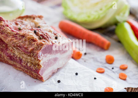 Geräuchertes Fleisch mit Gemüse auf braune Holztisch. geräuchertem rohen geschichtetes Fleisch mit rohen Kohl, grüne und rote Paprika, Karotten, Sonnenblumenöl zubereitet fo Stockfoto