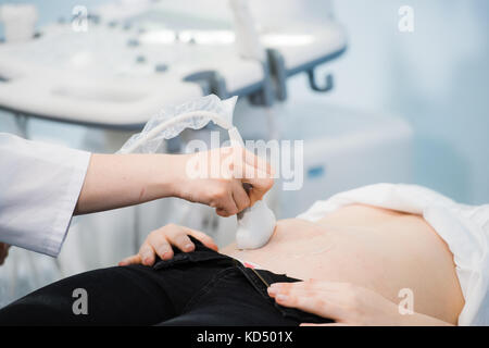 Nahaufnahme der inkognito Arzt mittels Ultraschall Geräte für das Screening von Schwangeren Frau und drücken Sie auf die Tasten des Computers. Frau Diagnose in der Klinik Stockfoto