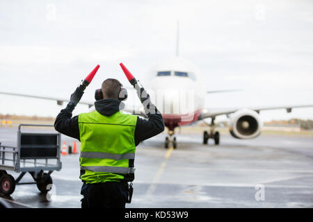 Ansicht der Rückseite des Bodenpersonals Signalisierung zum Flugzeug auf nasser Piste gegen Sky Stockfoto