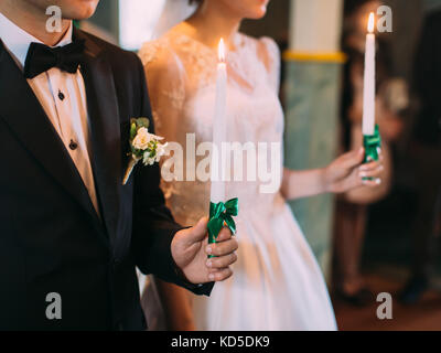 Die seitliche Ansicht der Hände der Jungvermählten' halten Sie die Kerzen mit grünen Bändern umwickelt. Trauung. Stockfoto