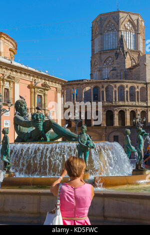 Foto des Touristen, Rückansicht einer Frau in einem rosa Kleid, die den Turia-Brunnen auf der Plaza de la Virgen im Zentrum von Valencia, Spanien, fotografiert. Stockfoto