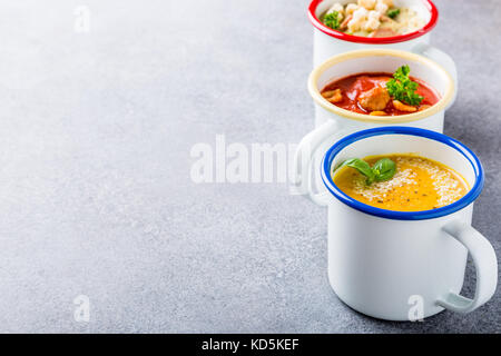 Verschiedene köstliche hausgemachte Suppen in Emaille Becher mit Zutaten. gesunde Ernährung Konzept mit kopieren. Stockfoto