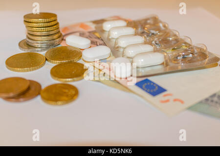 Weiß Tabletts mit Euro-Banknoten und -Münzen. Konzept der pharmazeutischen Unternehmen, Kosten für Gesundheit, Tiermedizin. verstreut Pillen. Stockfoto