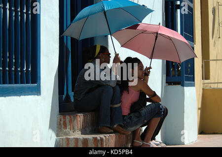 Kubanische junge Frauen sitzen auf der Treppe mit Sonnenschirmen für Schatten, Camagüey, Kuba Stockfoto