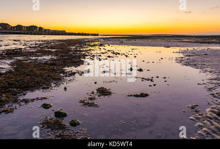 Ein Strand kurz vor Sonnenaufgang mit orange Wolken im Wasser übrig gebliebene Reflektieren von das Meer bei Ebbe, in Großbritannien. Stockfoto