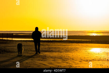 Silhouette eines Mensch und Hund am Strand, wenn die Sonne aufgeht in Großbritannien. Stockfoto