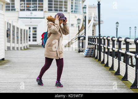 Frau kämpfen in den Wind zu gehen, während Ihr Hut Festhalten am Pier in Worthing Worthing, West Sussex, England, UK. Stockfoto